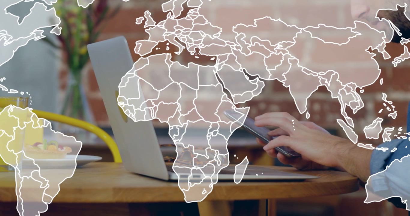 Man using laptop, phone at cafe, world map fading in overlaying table to show tech network
