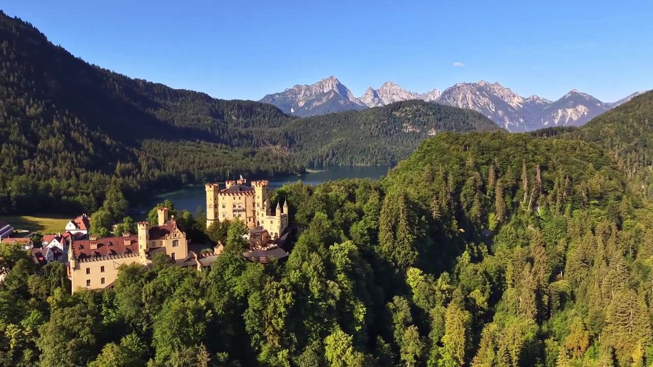 Vista aerea con drone del Castello di Hohenschwangau sopra il lago Alpsee con le Alpi in lontananza, Schwangau, Germania