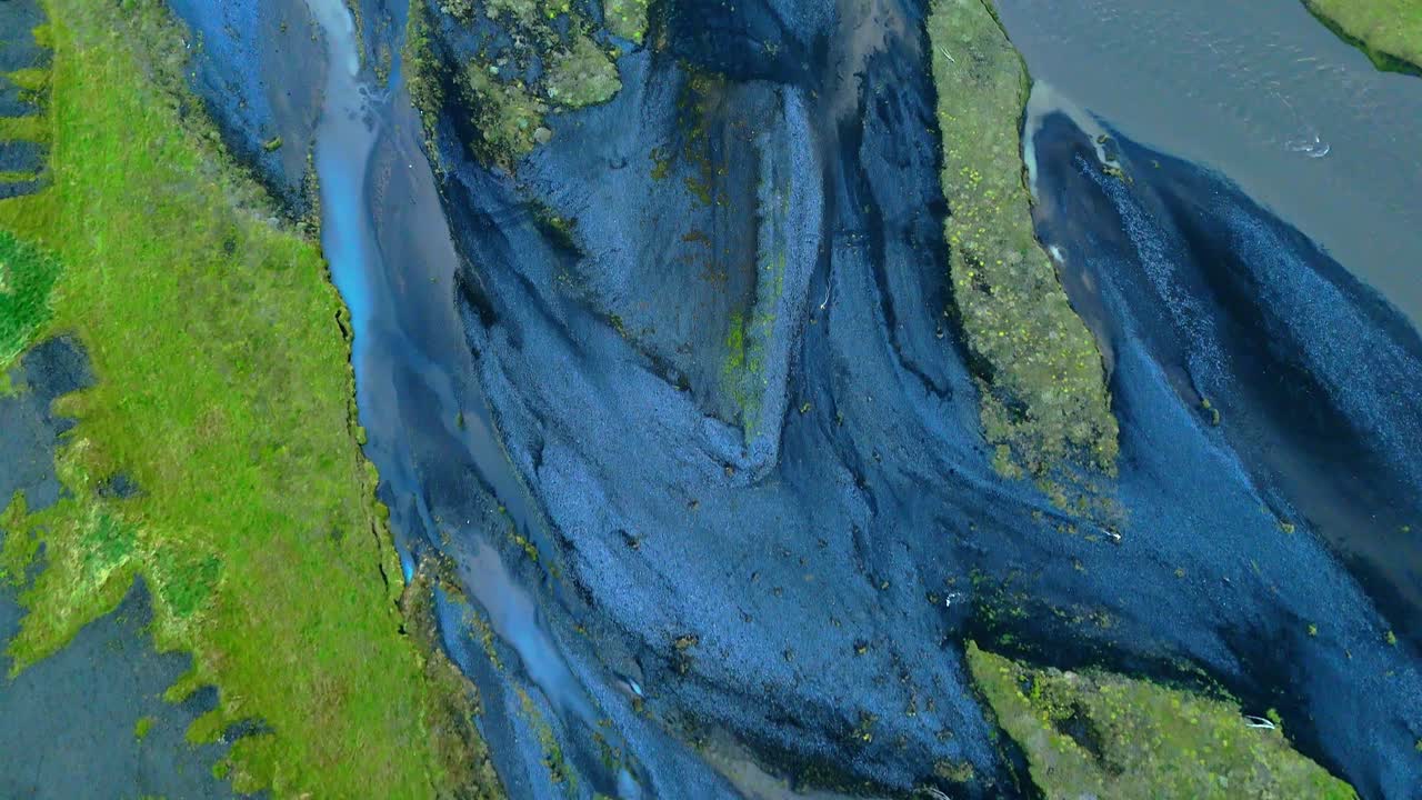 Icelandic streams twist like veins on their journey through glaciated valleys, volcanic rock and vibrant mossy greens and aqua pools making patterns to the sea. Drone aerial reveal horizon