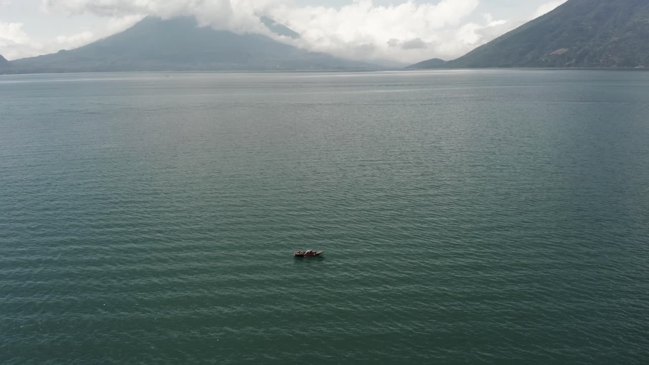 hombre remando en bote en el lago de atitlán con el volcán san pedro en el fondo, guatemala