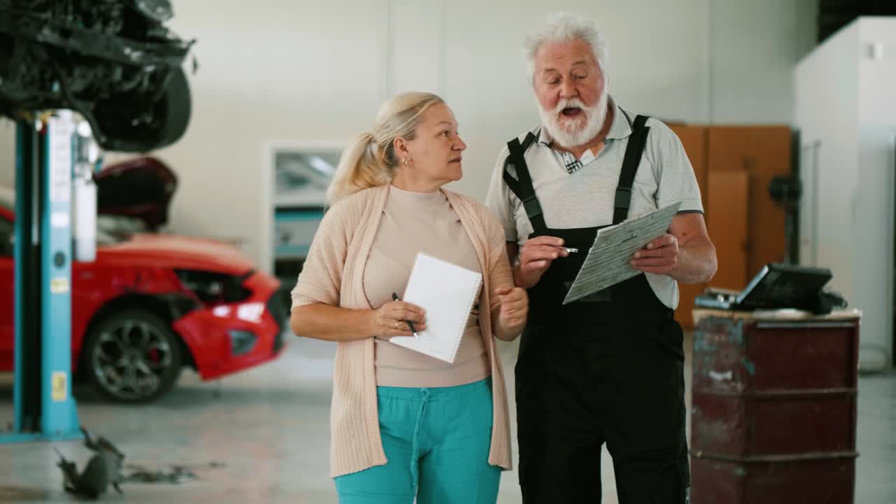 un viejo mecánico y un agente de seguros visitan coches dañados en un taller de reparación