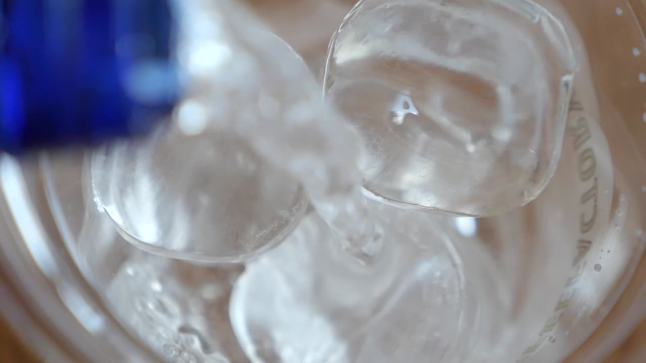 Pouring liquid over ice cubes in a glass