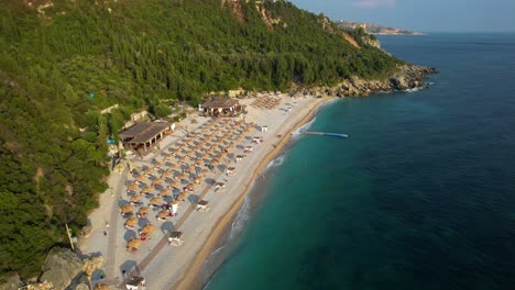 pristine beach with white sand and crystal blue sea, surrounded by green hills, beach bars, and umbrellas