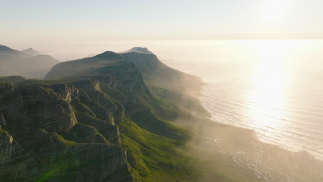 Breath-taking-romantic-aerial-shot-of-mountains-at-sea-coast.-View-against-sun-at-golden-hour.-Mountain-ridge-towering-above-shore.-Cape-Town,-South-Africa