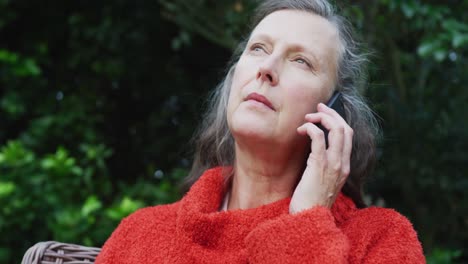 happy senior caucasian woman sitting in garden, looking around and talking on smartphone