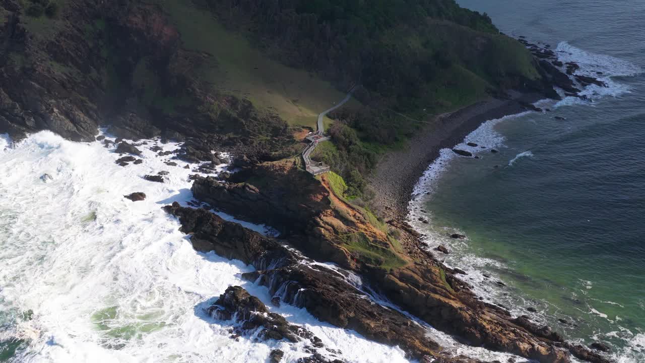 Dynamic aerial footage of waves crashing against Byron Bay's rocky coastline, showcasing the natural beauty and power of the ocean