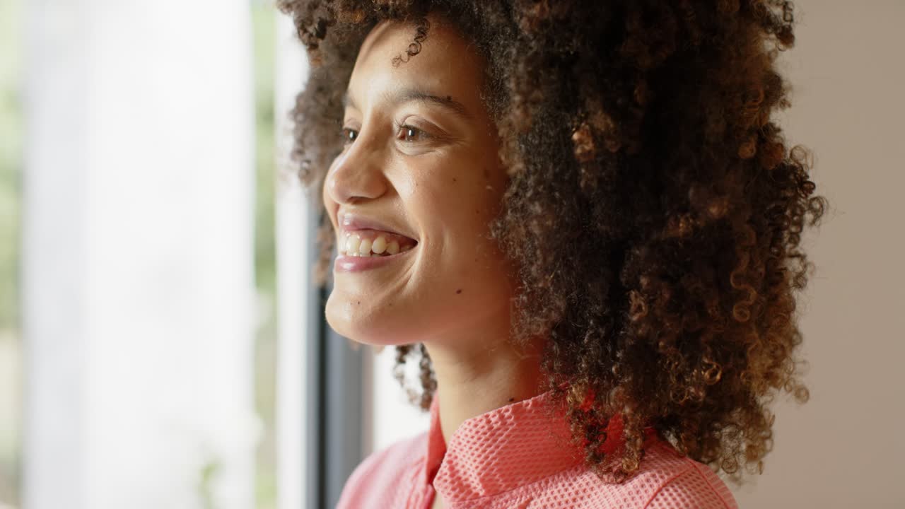 Woman gazing out through big glass window, smiling in sunlight and appreciating foliage, copy space