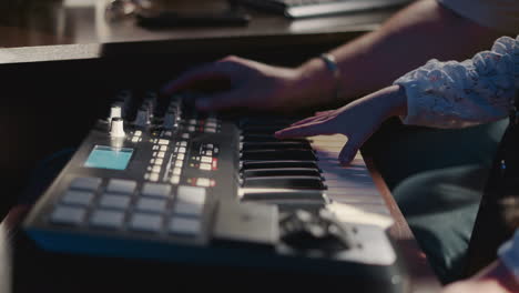 child plays synthesizer with teacher in studio closeup. little girl learns digital musical instrument while mentor setups console in class. music art