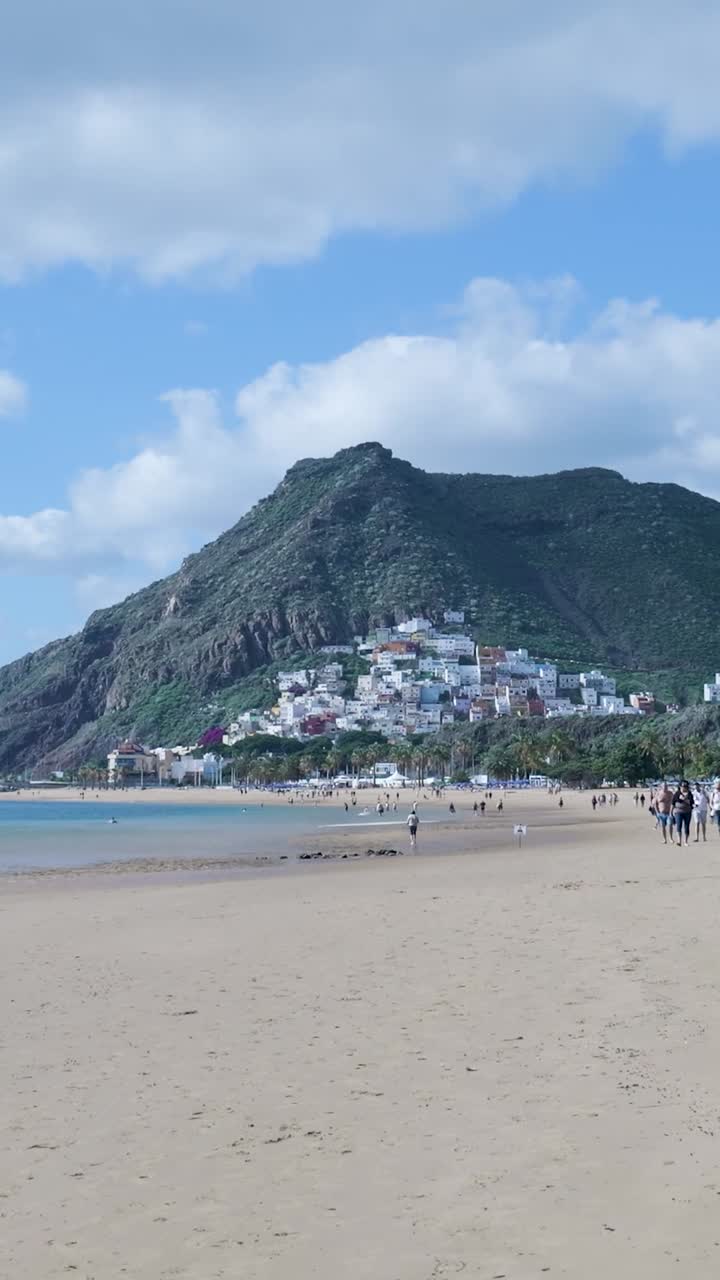 Spiaggia panoramica con cittadina costiera adagiata ai piedi di una montagna verde