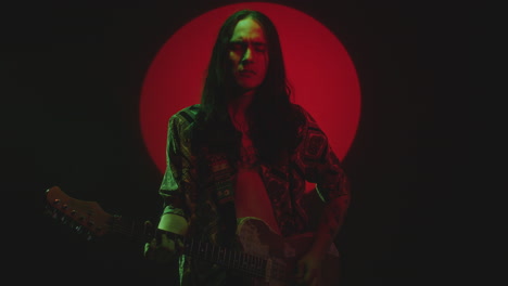 young music artist playing guitar with eyes closed in red spotlight