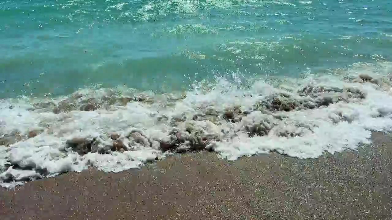 Le onde si infrangono dolcemente sulla riva in una località balneare durante una giornata di sole.