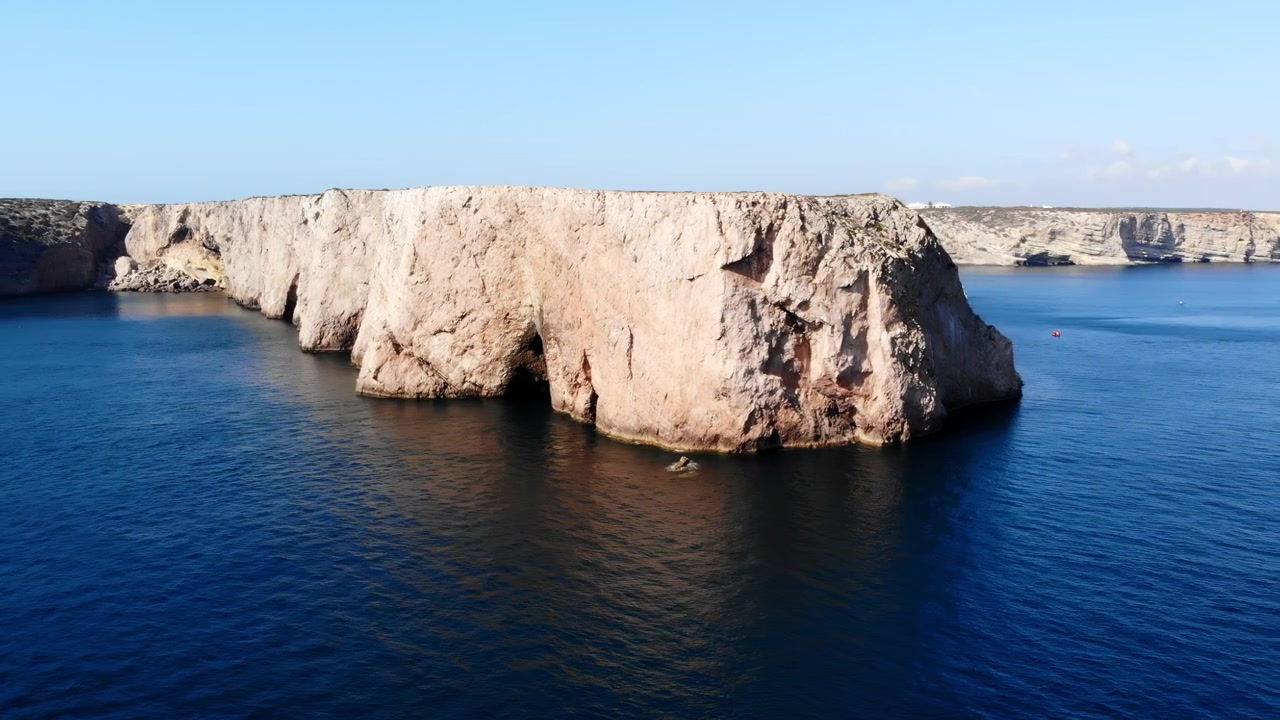 Ampia vista aerea di una scogliera calcarea chiara o di una piccola isola circondata da acque blu aperte sotto un cielo sereno, con una luminosa luce diurna naturale e un'atmosfera pacifica.