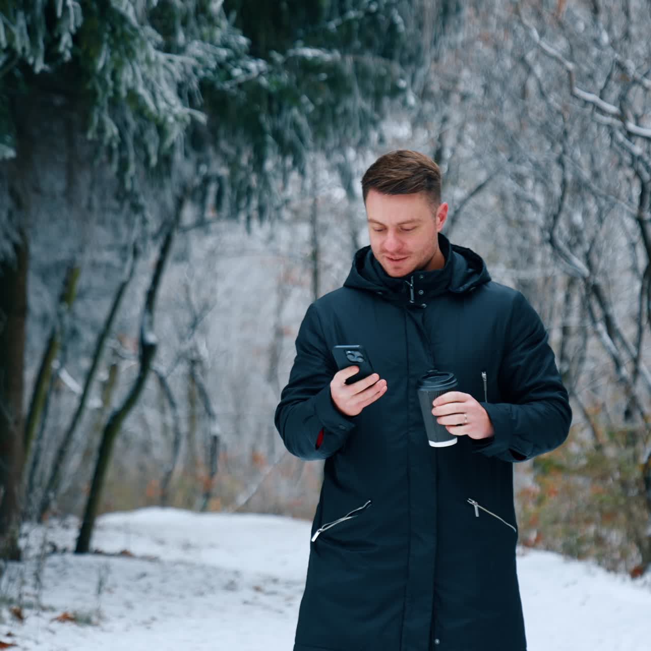 Uomo sicuro di sé in giacca nera che guarda il suo telefono. L'uomo beve caffè concentrato sul suo smartphone. Giornata invernale sullo sfondo.