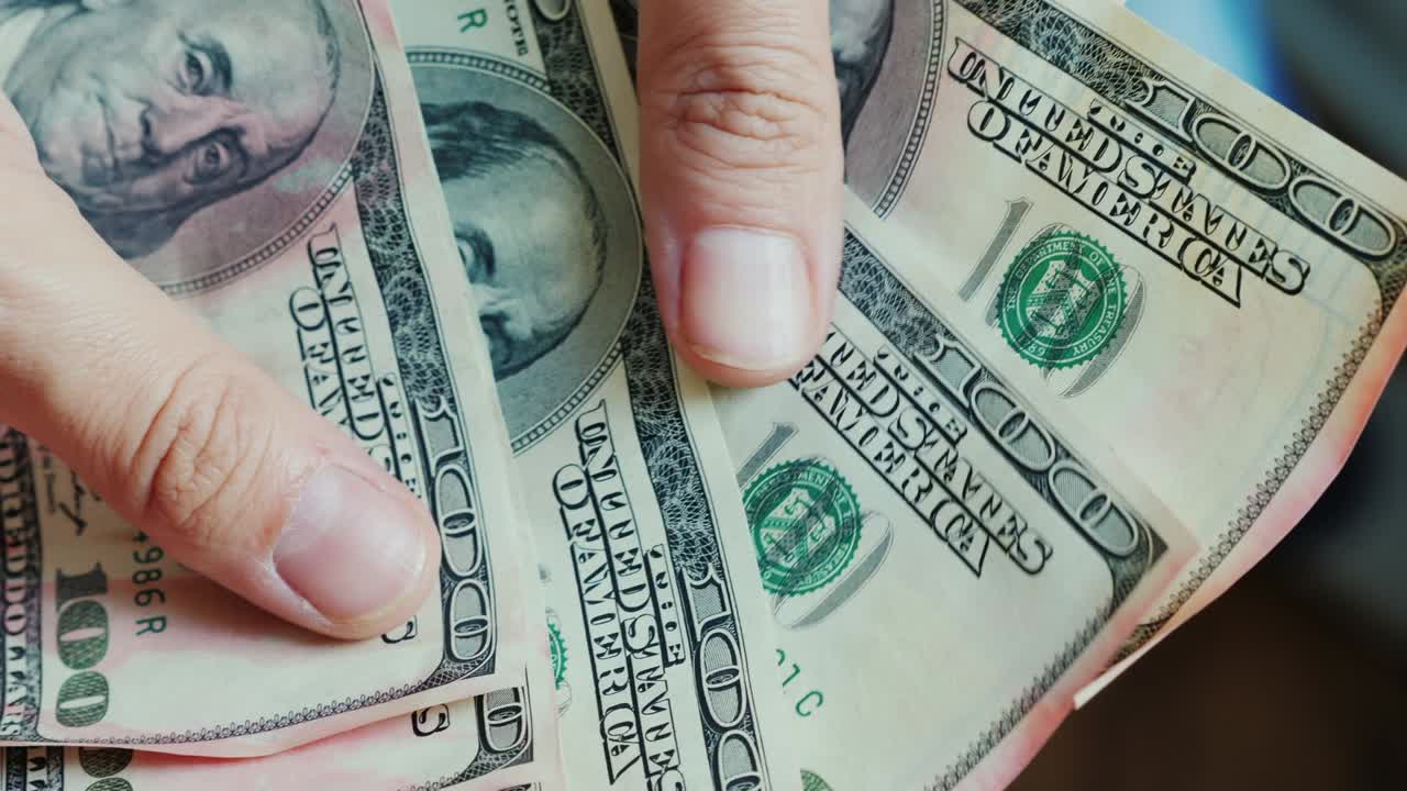 los dedos de los hombres miran los billetes de dólares estadounidenses. el dinero está dañado por la pintura rosa.