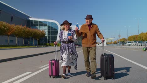 stylish retired family couple granny grandfather walking with luggage suitcase bags to airport hall