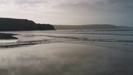 The-tide-coming-in-across-a-sand-and-pebble-beach-in-Broad-Haven,-West-Wales-in-early-evening