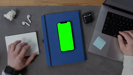 person working on laptop with mockup green screen smartphone