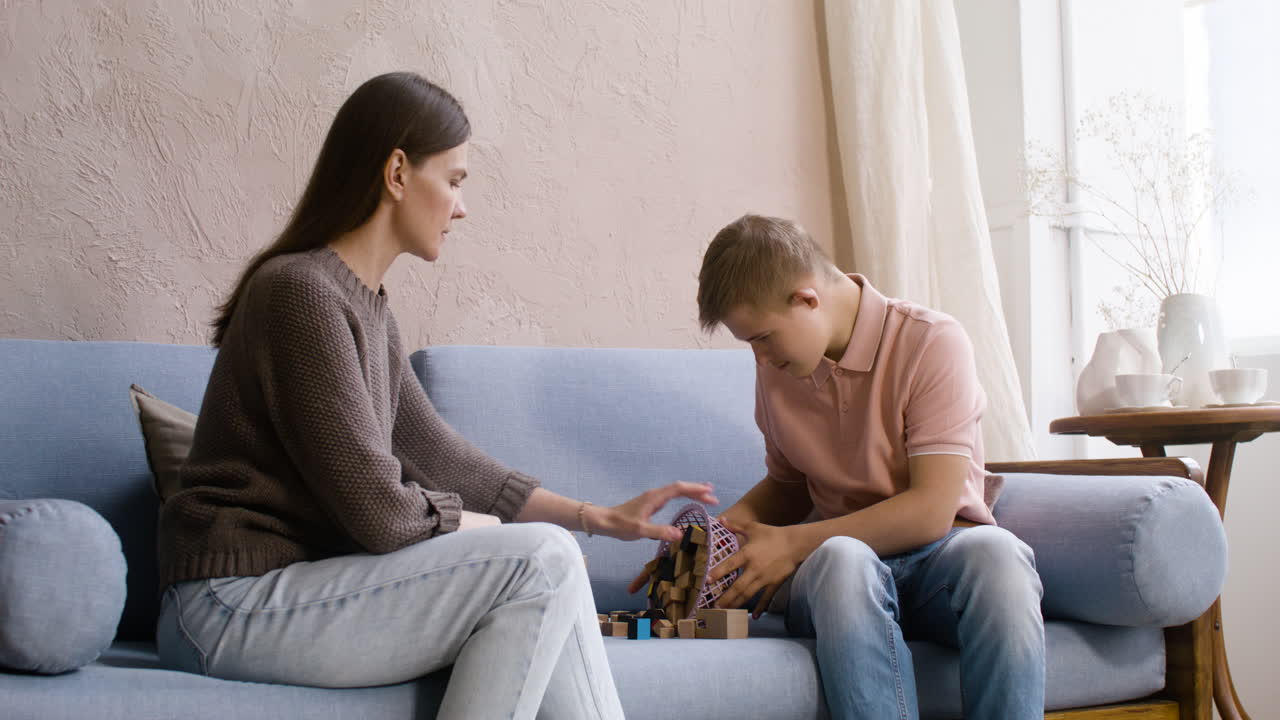 niño con síndrome de down y su madre jugando con cubos de madera en el sofá de la sala de estar en casa