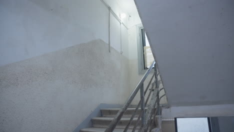 man hurries down sketchy stairwell, holding a suitcase tightly, protecting something precious, classified files. running away or being chased. escape, secrecy, and underground dealings. spy or thief.