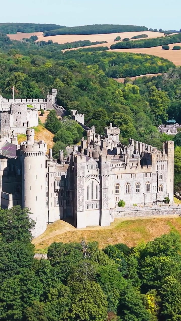 L'orbita del drone sul Castello di Arundel rivela una fortezza medievale in pietra, torri e mura sopra un parco boscoso nel West Sussex, Inghilterra, in una limpida giornata estiva con dolci colline sullo sfondo. Formato verticale