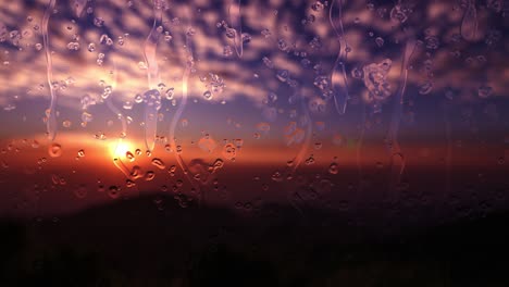 water drops on a window glass when raining. the sky with clouds and sun set on background. drops of rain flow down the glass in the evening sunset.