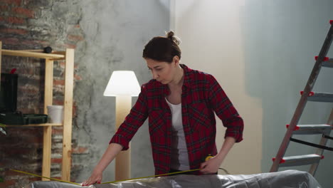 thoughtful woman measures sofa with retractable tape in room