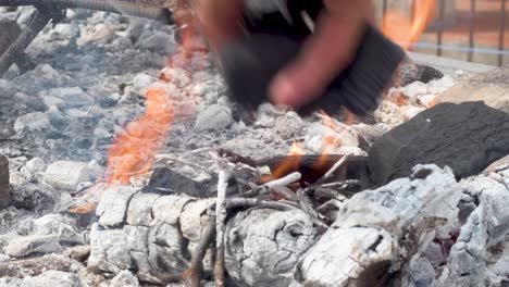 hand places charcoal to feed the fire of a barbecue