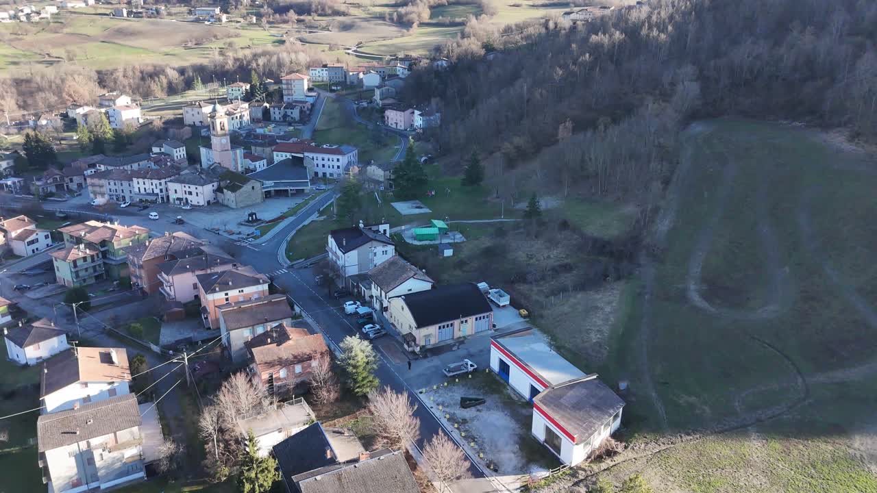 Villaggio di Morfasso circondato da boschi spogli e campi agricoli a fine inverno nella Val d’Arda, Provincia di Piacenza, Emilia-Romagna, Italia — ripresa aerea lenta.