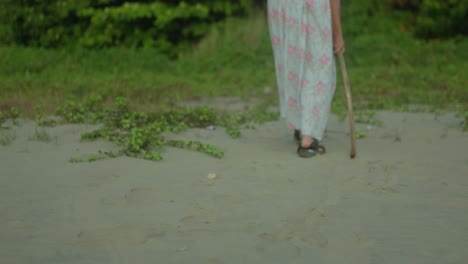 woman with a cane walking on a sandy path in daylight, close-up on feet