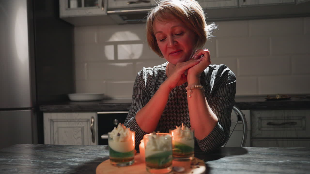 Light switched off, candle placed on table casting warm glow as chef admires her artistic dessert creations, radiating pride and calmness in cozy kitchen atmosphere filled with culinary passion