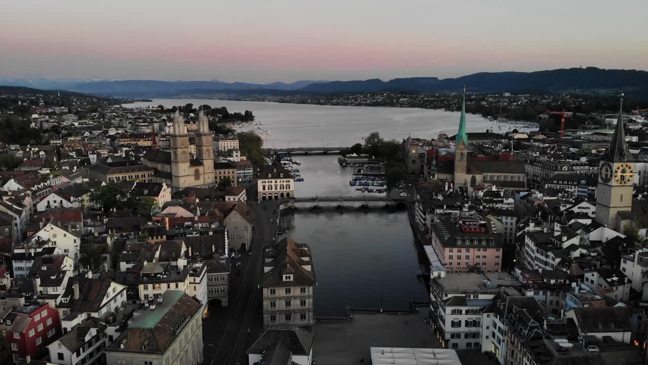 Aerial flyover over Limmat river in Zurich, Switzerland at dusk from Altstadt to Lake Zurich with views of Grossmünster, St. Peter, Frauenkirche