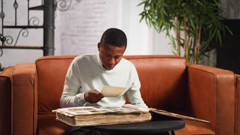 doubting guy looks at old relatives pictures on small sofa