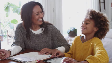Frau-Mittleren-Alters-Und-Enkelin-Machen-Gemeinsam-Hausaufgaben-Mit-Einem-Tablet-Und-Lachen,-Nahaufnahme
