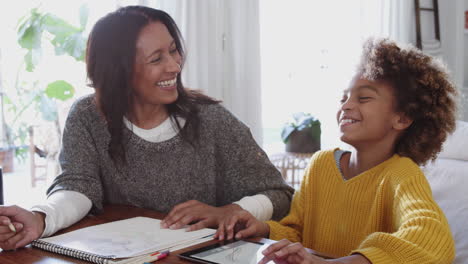 Mujer-De-Mediana-Edad-Y-Nieta-Haciendo-Los-Deberes-Juntas-Usando-Una-Tableta-Y-Riendo,-De-Cerca