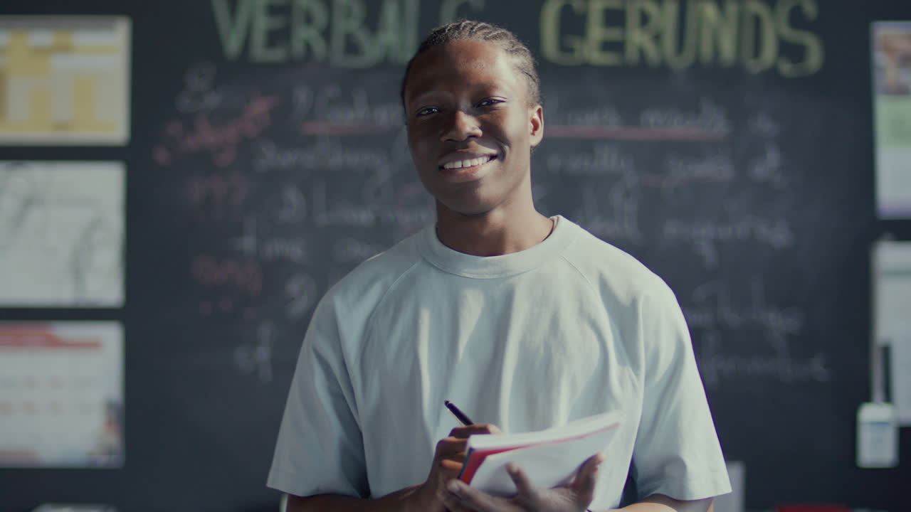 Portrait of Happy African American Student with Pen and Notebook in Classroom