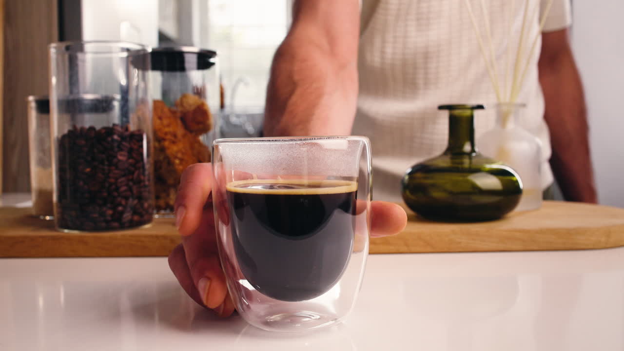 Mano che appoggia una tazza di caffè appena fatto sul bancone della cucina