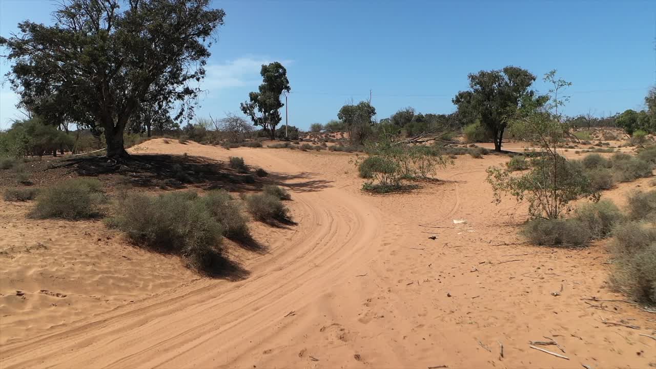 Volo di drone in stile FPV a bassa quota lungo un sentiero sabbioso attraverso un paesaggio arido con cespugli vicino ad Agadir, Marocco