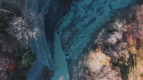 aerial view above a blue river in middle of leafless, foliage forest, sunny, fall day - rising, top down, drone shot