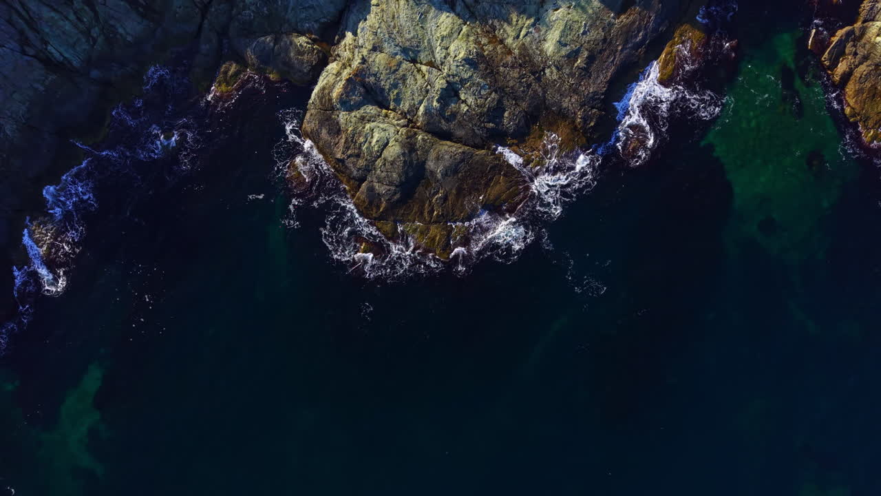 Nature's tranquility wraps around coastal rocks as waves dance rhythmically, creating a serene scene at sunset by the shore