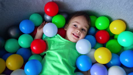 happy smiling toddler lies in the dry pool. charming caucasian baby boy in a pile of colorful balls.