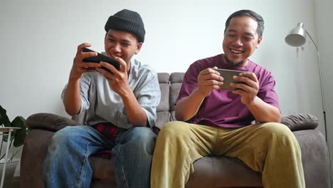 two men playing mobile games on a couch