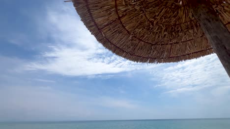 Wide-angle-tilt-down-panorama-of-wattled-straw-beach-umbrella-to-beach-and-sea-view