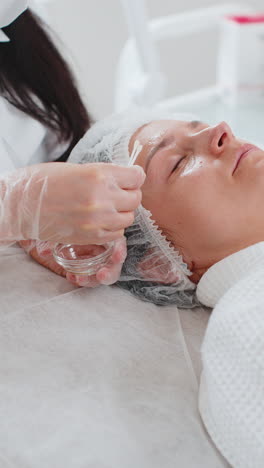esteticista aplicando hidratante química médica peeling máscara de ácido en la cara y los ojos de una mujer joven