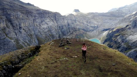 A-hiker-running-towards-a-viewpoint-over-lake-Limmernsee-in-Glarus,-Switzerland,-the-turquoise-colored-water-of-which-is-surrounded-by-tall-Swiss-Alps-peaks-and-cliffs