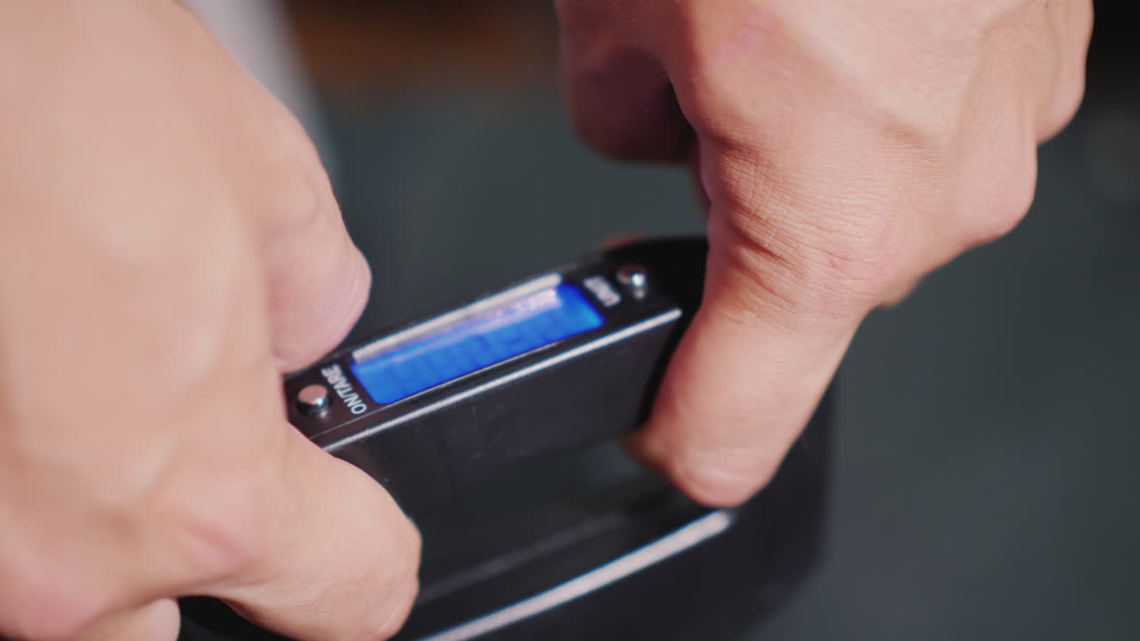las manos de un hombre sostienen básculas de carretera que pesan equipaje antes de viajar