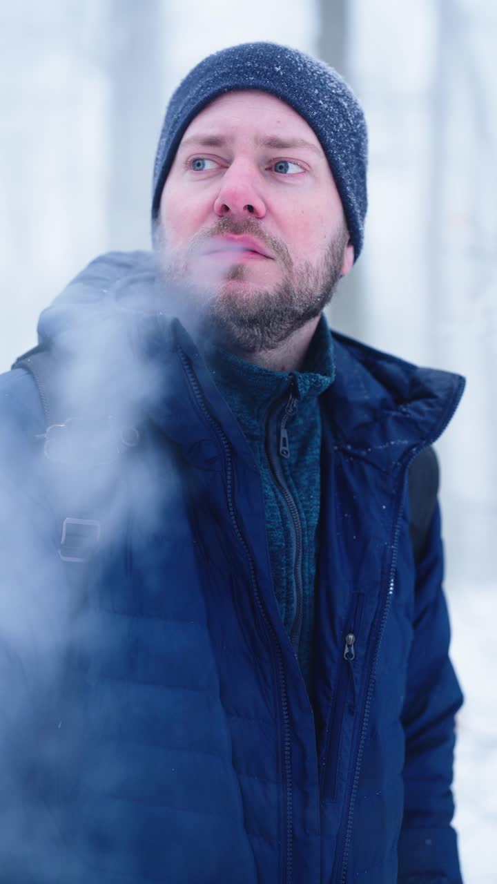 Lodret slow motion-video af en mand, der vaper en elektronisk cigaret i en kold vinterskov. Tyk damp-sky i den frysende luft skaber et dramatisk sæsonbestemt udendørsportræt