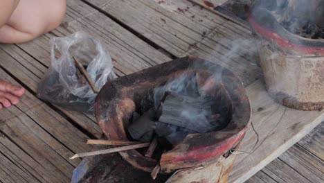 close-up of an individual replenishing charcoal in a classic thai earthen stove with smoldering embers for grilling