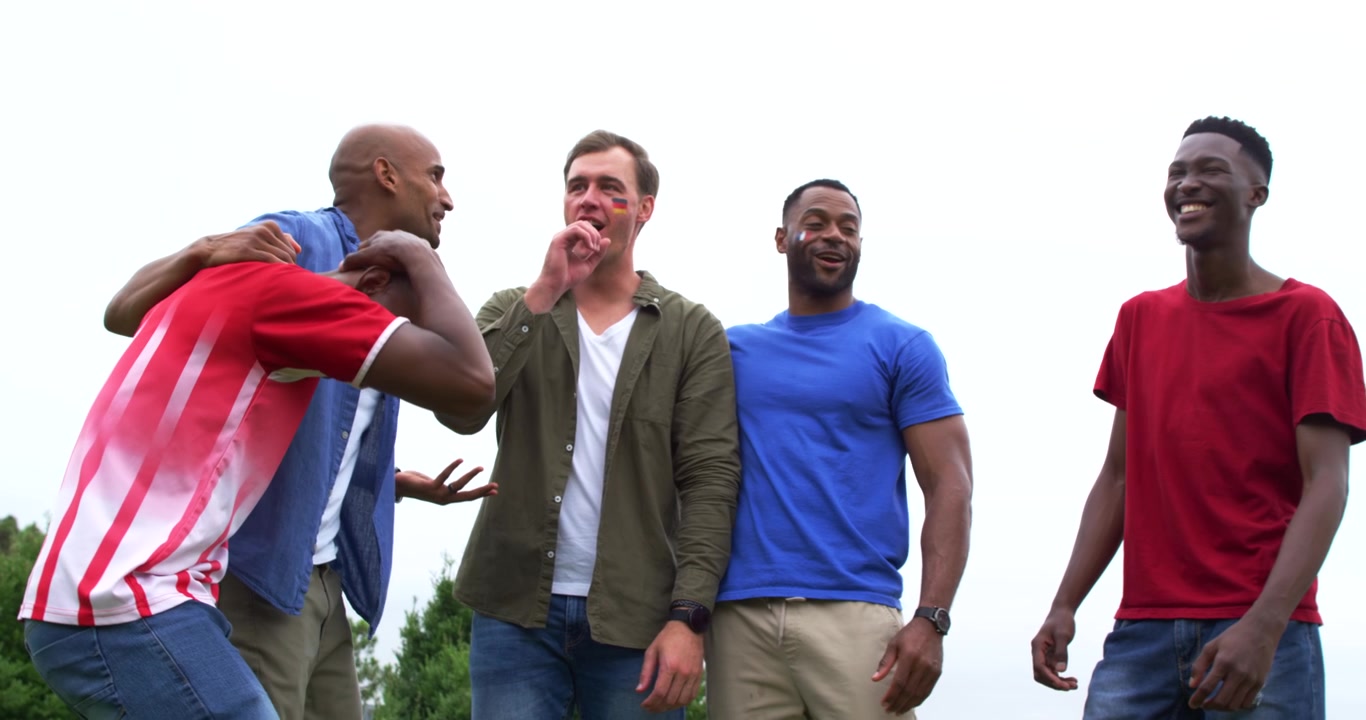 Male friends walking toward lens in park second man teasing, center man laughing with face sticker