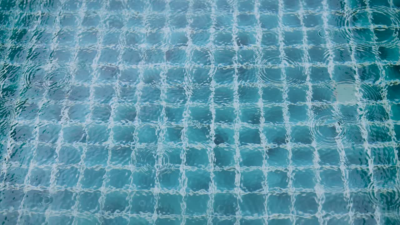 부드러운 조명으로 찍은 타일로 된 수영장 표면에서 파동을 일으키는 방울의 조용한 풍경