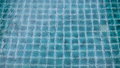 a serene view of raindrops creating ripples on a tiled pool surface, captured in soft lighting